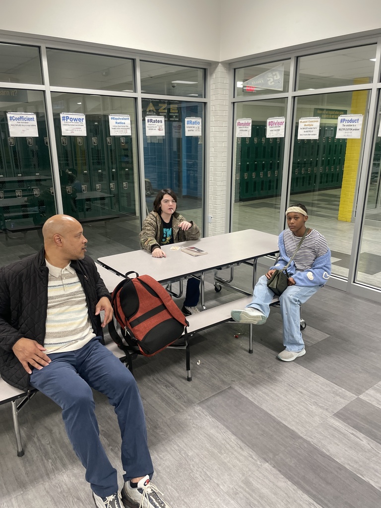 1 man or volunteer sitting in cafeteria with two students.