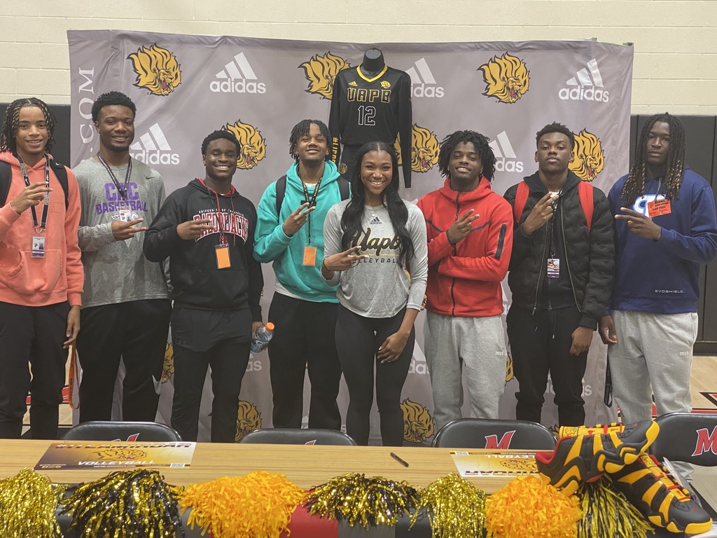 A woman surrounded on each side by boys. She and they are smiling