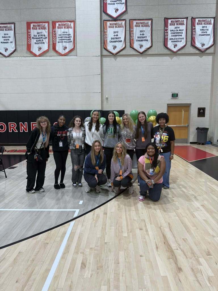 Gracie Keeling in a PJC softball sweatshirt in front of a table of cupcakes balloons and softball paraphernalia.  She is surrounded by other school age girls.