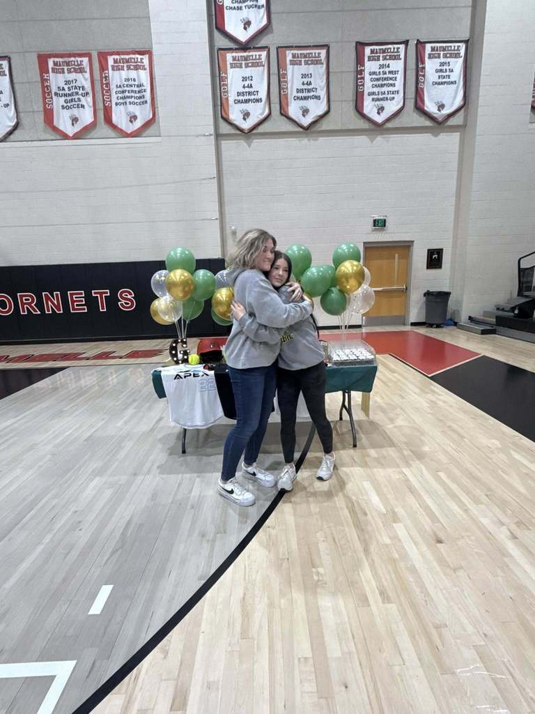 Gracie Keeling in a PJC softball sweatshirt in front of a table of cupcakes balloons and softball paraphrenalia. She is hugging an older woman.