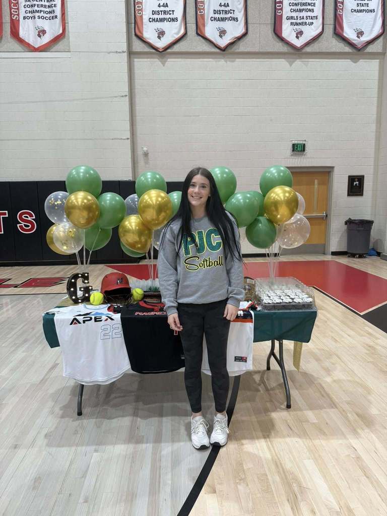 Gracie Keeling in a PJC softball sweatshirt in front of a table of cupcakes balloons and softball paraphrenalia