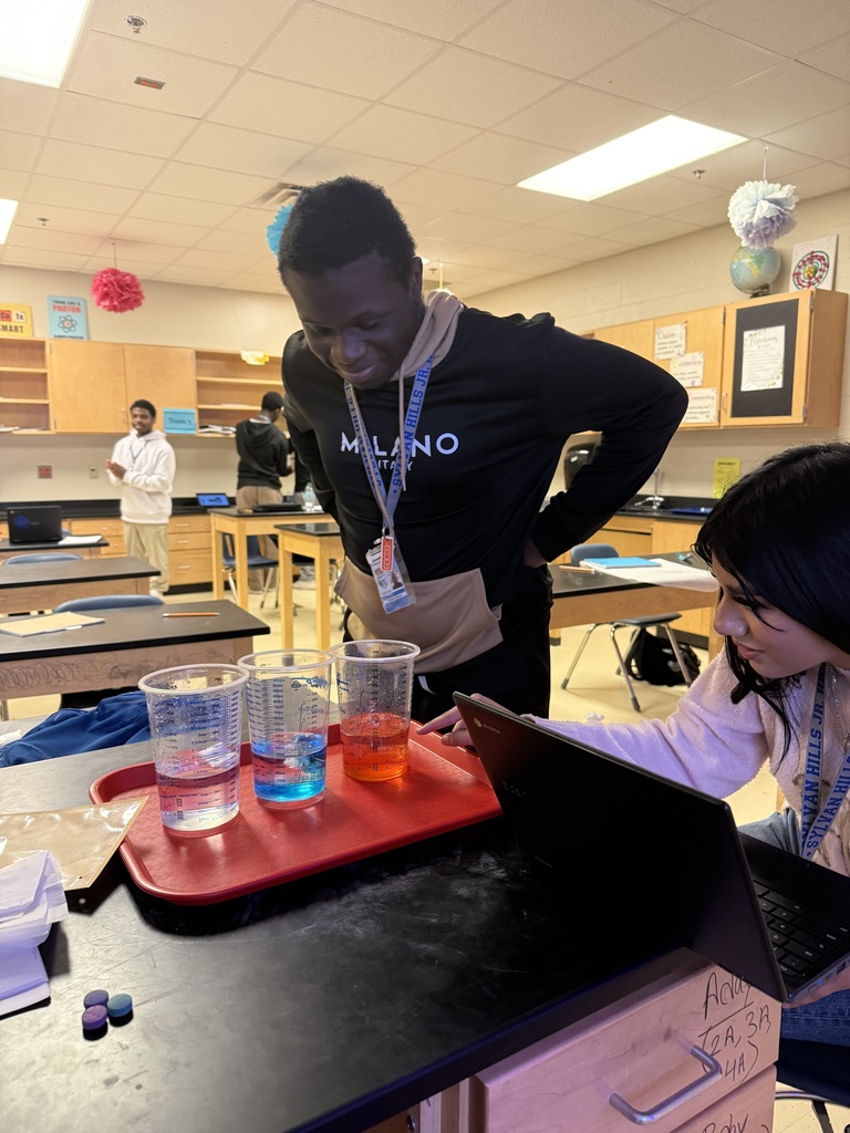 A classroom setting with two students in an experiment involving colored liquids on a red tray.