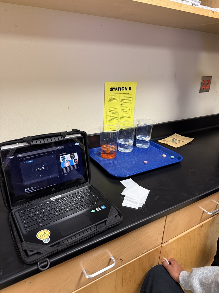 Laptop with keyboard, glasses, papers, and a sign on the wall labeled "Station 5".