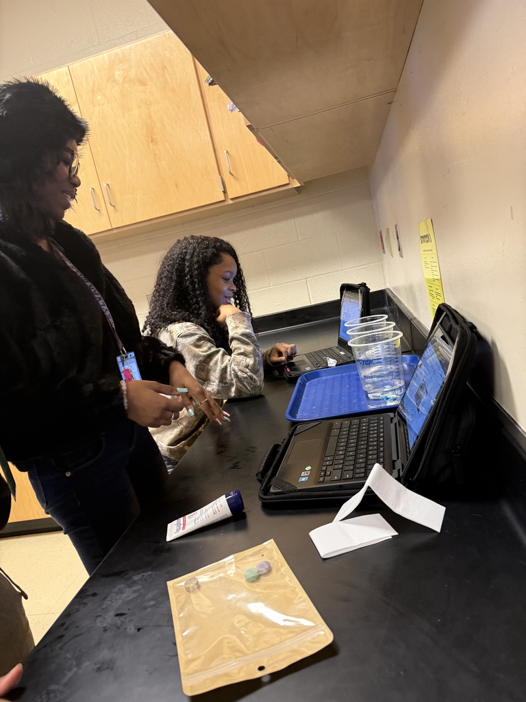 Two individuals, one male and one female, working at a workspace with a laptop, papers, and other items on the table.