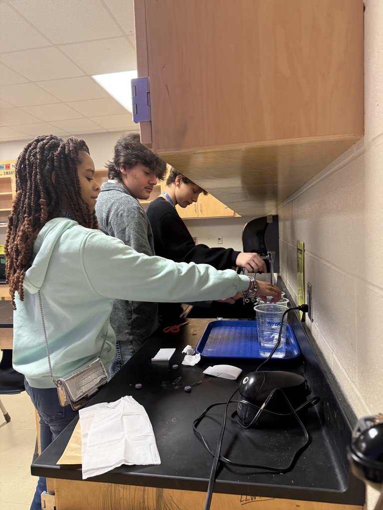 Three people, two women and one man, standing at a counter using electric appliances in what appears to be a lab area.