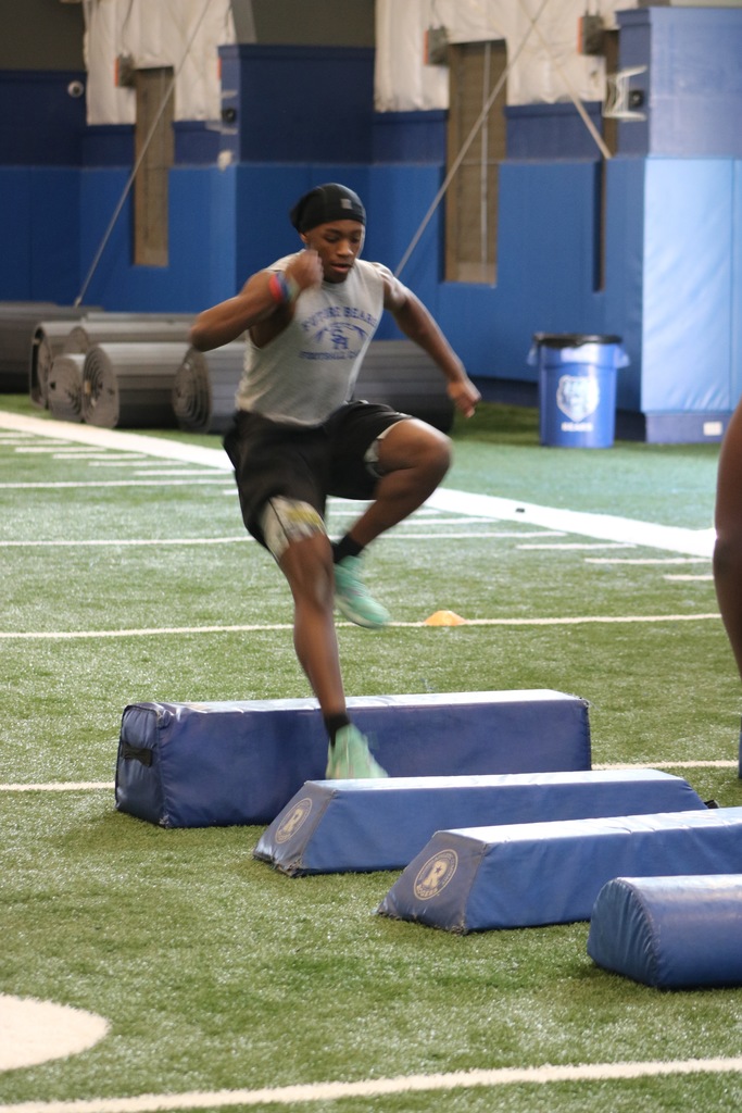 A student hurdling small blue things on an indoor practice field