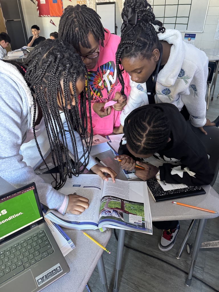 Four girls leaning in to read a book. 