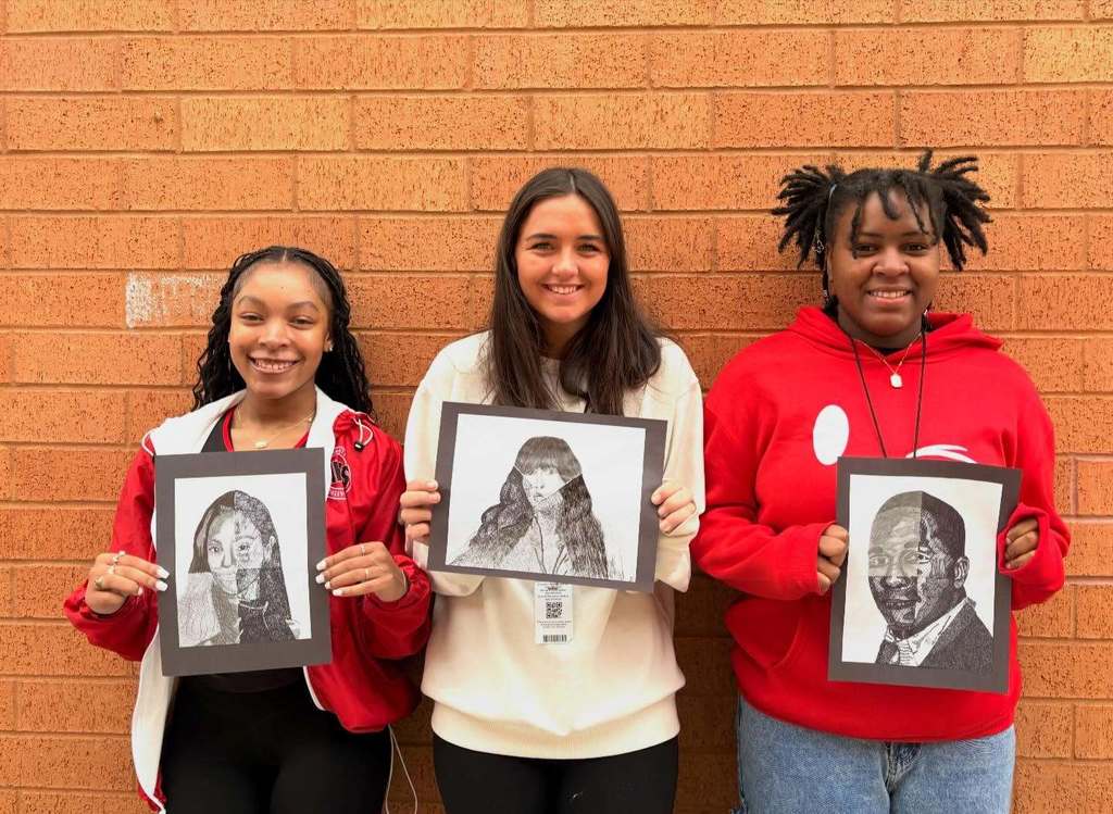 Three students smiling while holding their celebrity portraits