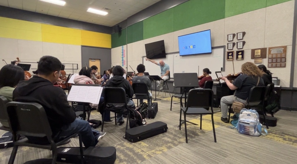 Orchestra teacher leading rehearsal with students