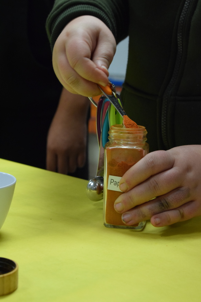 A close up of a student using measuring spoons with paprika