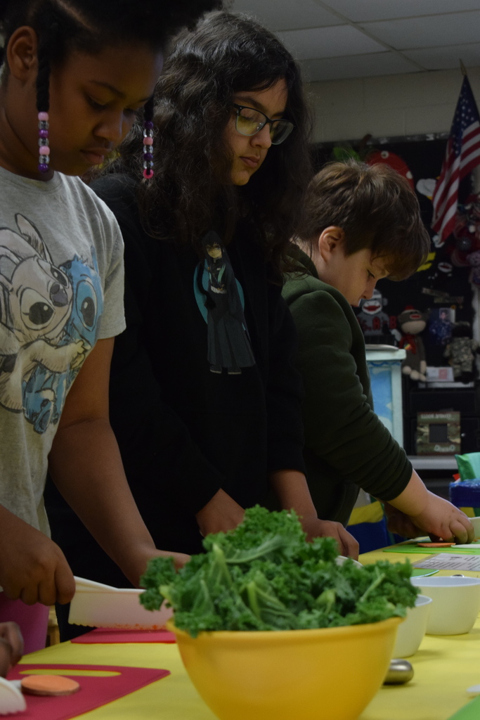 Students cutting at a table with kale in the foreground