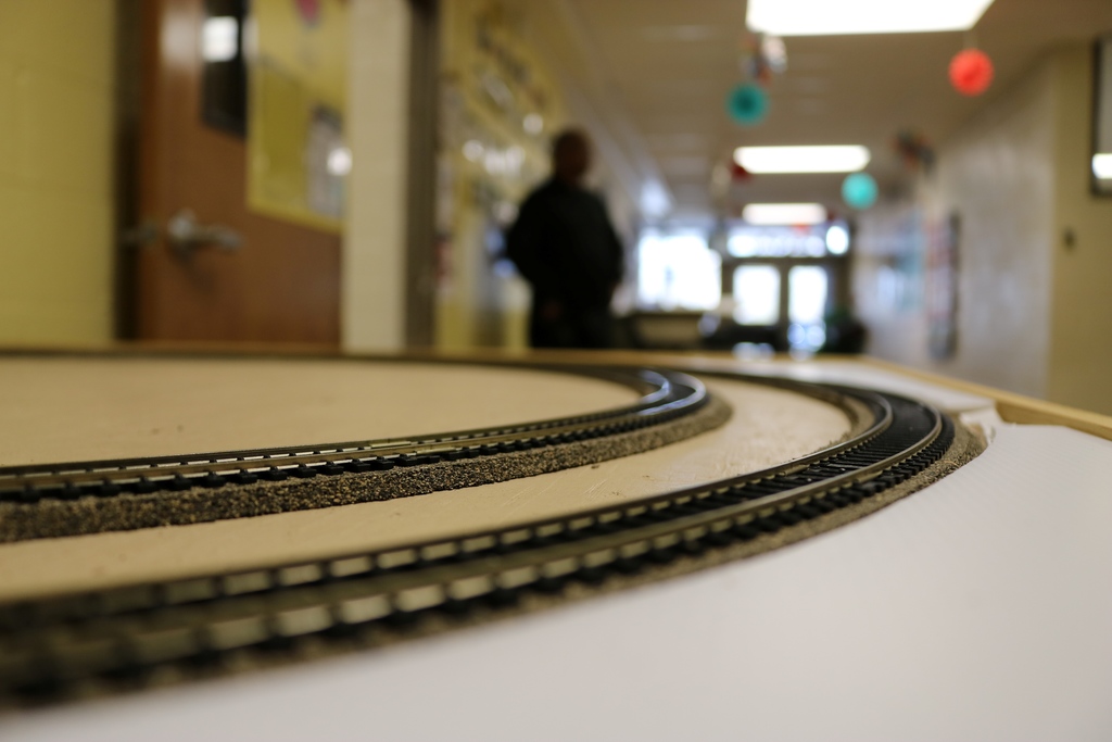 Train tracks in focus in the foreground. The background is blurry with a silouette and a school entrance