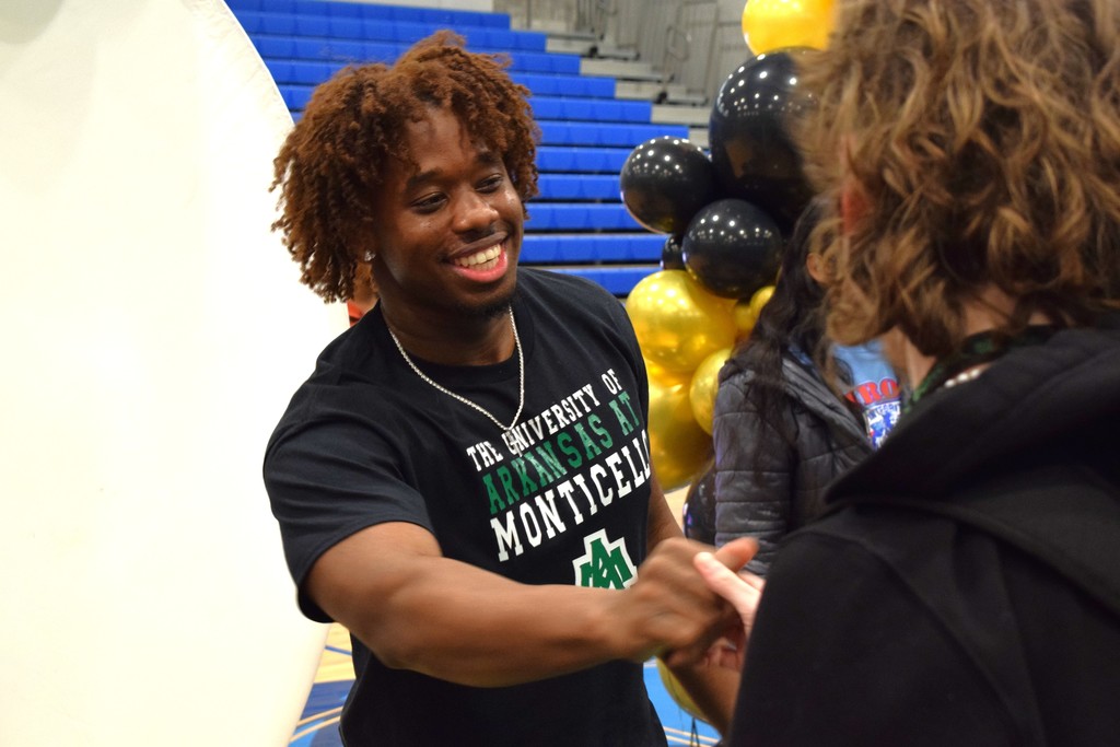 A smiling athlete in a University of Arkansas at Monticello shirt smiles as she shakes someone's hand