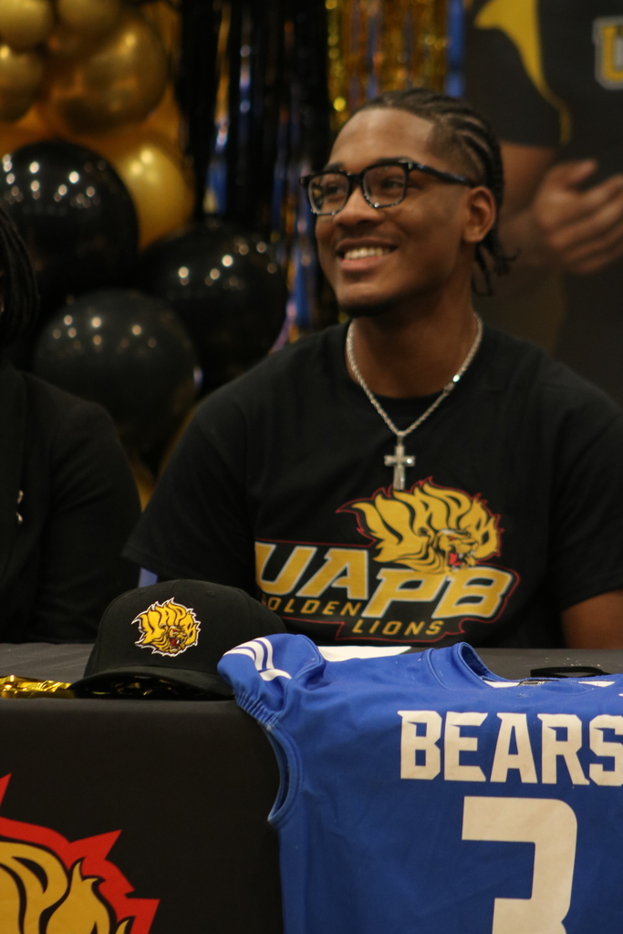 A student smiles brightly after signing to play football with UAPB Golden Lions. He is wearing a cross necklace.