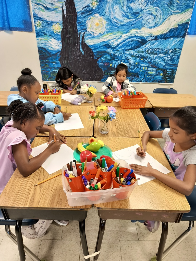 2nd grade practice Still Life drawings. Several students with pencil and paper sitting at a table drawing fruit and flowers.