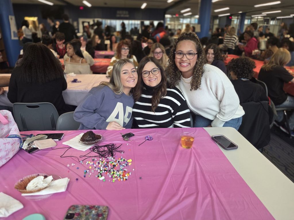 A picture of three women smiling together at a table while working on a craft