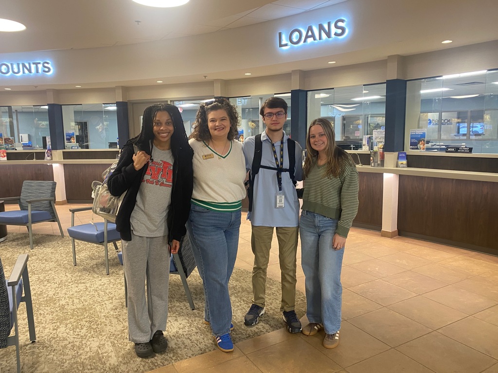 Four people standing in a bank lobby. Neon signs say "accounts" and "loans" in the background