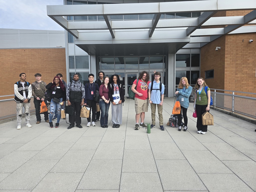 Students stand in front of Maumelle High School. One is giving bunny ears to his classmate