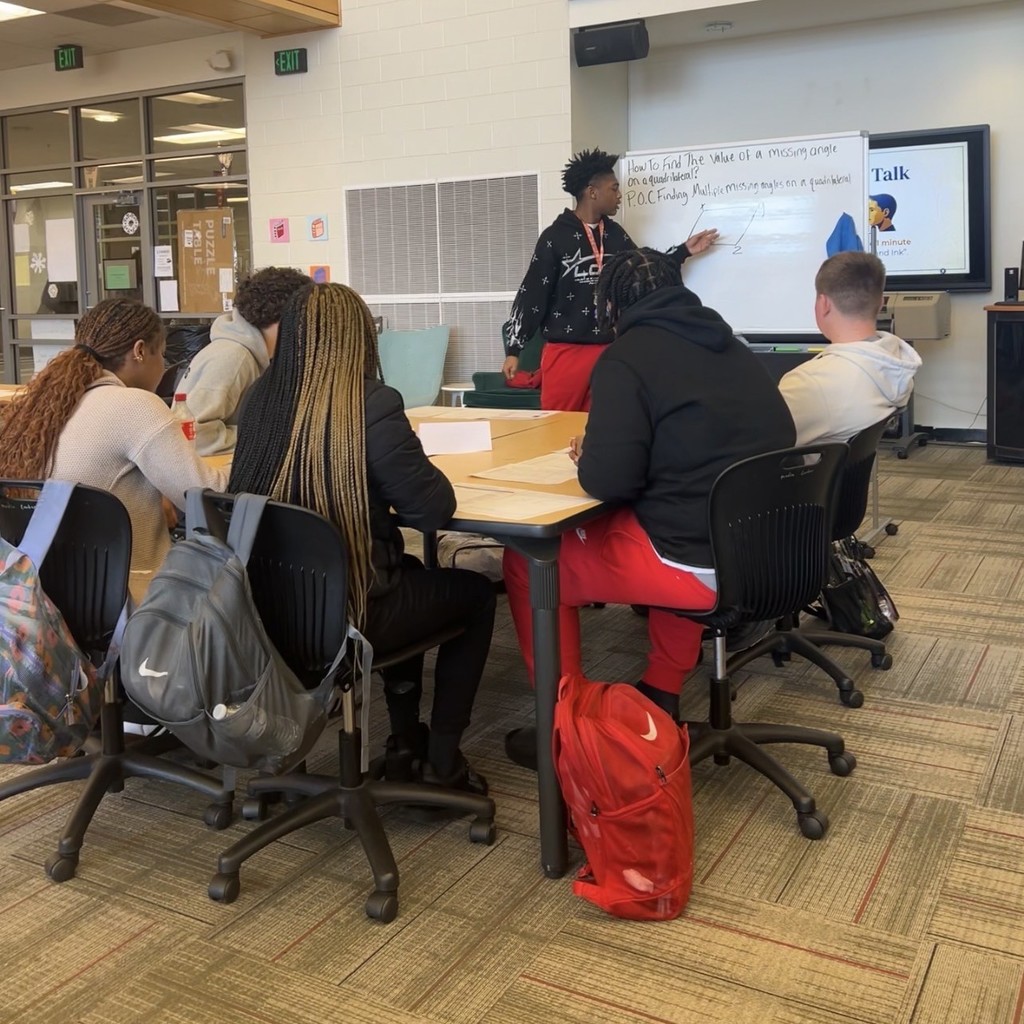 Maumelle High School 9th grade AVID I students showcasing AVID tutorial strategies for all secondary principals and AVID coordinators in the district. One student is using a whiteboard while many look to him in the library