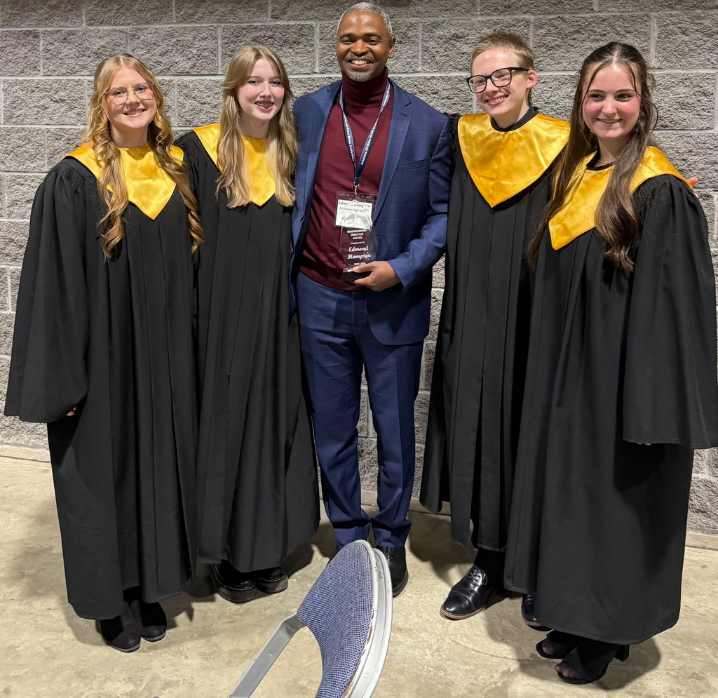 Edmond Hampton holding his choral director of the year award with two students on either side of him smiling.