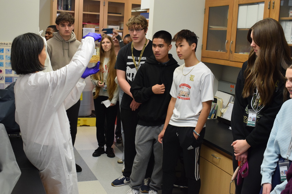 Joe T. Robinson High School Health Science Pathway is learning about bacteria from a a woman in a lab coat holding a glass jar.