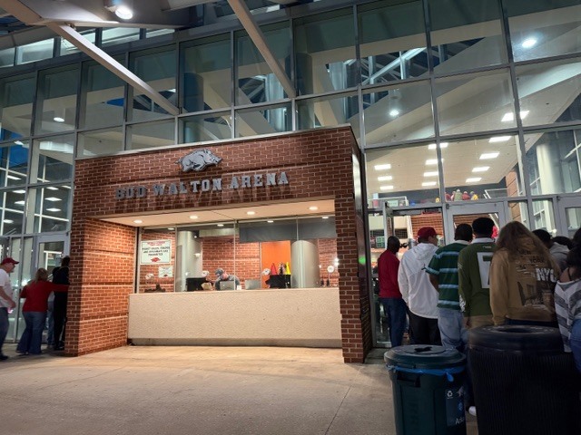 The exterior of Bud Walton Arena with the ticket booth and a line at the door