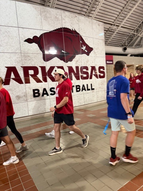 Students walking in front of a sign that says "Arkansas Basketball" with a Razorback logo above it