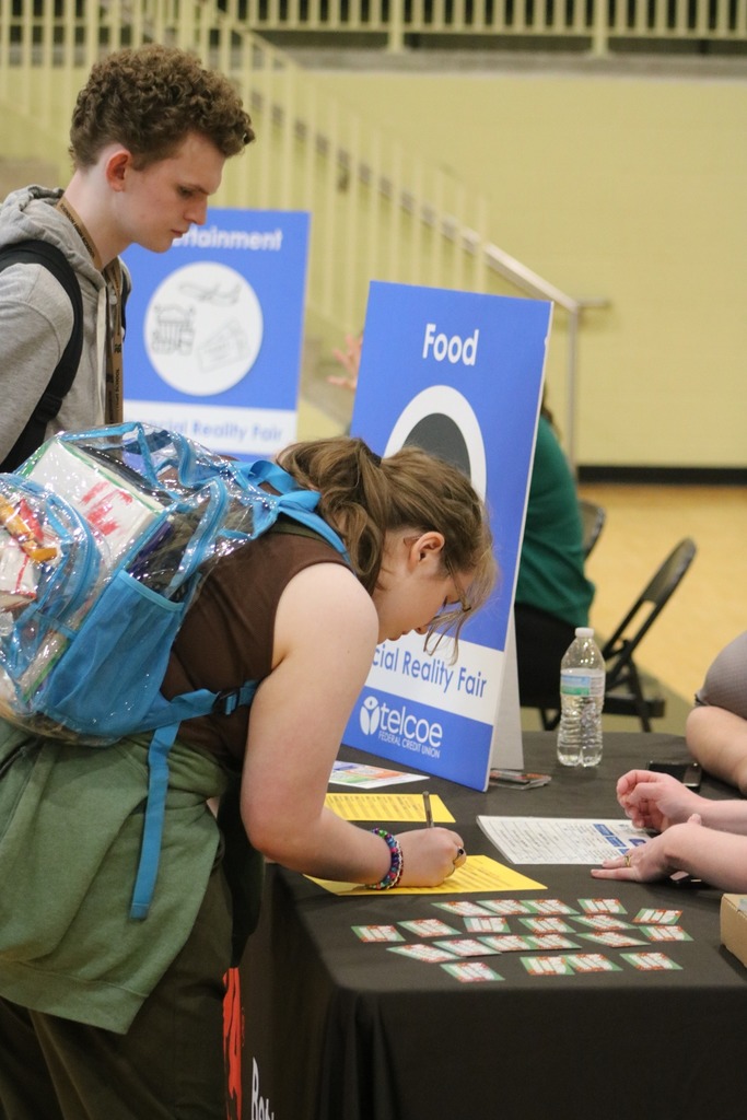 A girl wears a backpack while budgeting for food at a table.