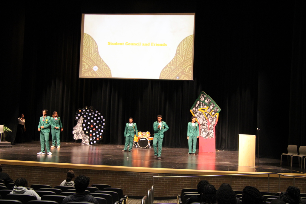 Boys stand on a stage for some kind of performance. The projector slide says student council and friends