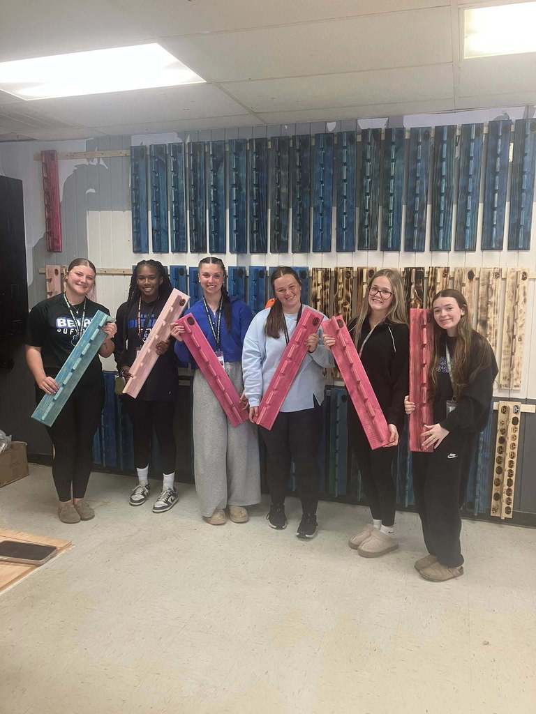 Six girls holding hat racks posed side by side in front of many more hat racks.