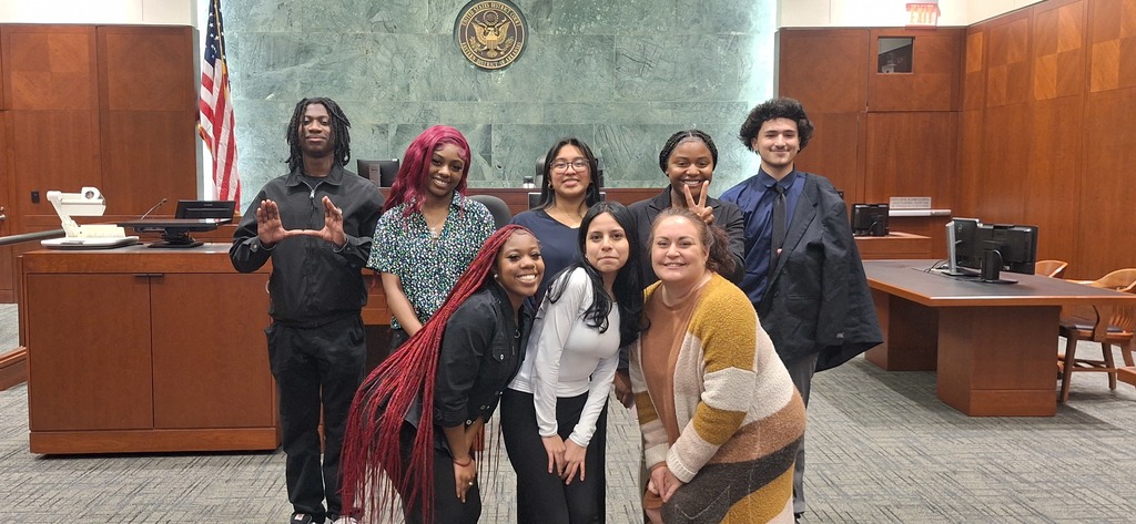 A group photo inside a courtroom. There are seven people in the photo. Five in the back. Three in the front.