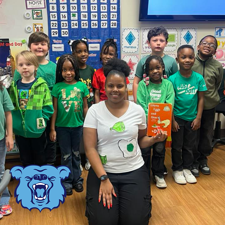 Sherwood Elementary students and their teacher smiling and dressed for "Green Eggs and Ham". Their teacher is holding the book.