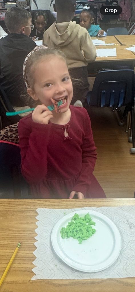 A smiling student in a maroon dress sits at her desk, holding a teal fork with a bite of ham as she prepares to eat.