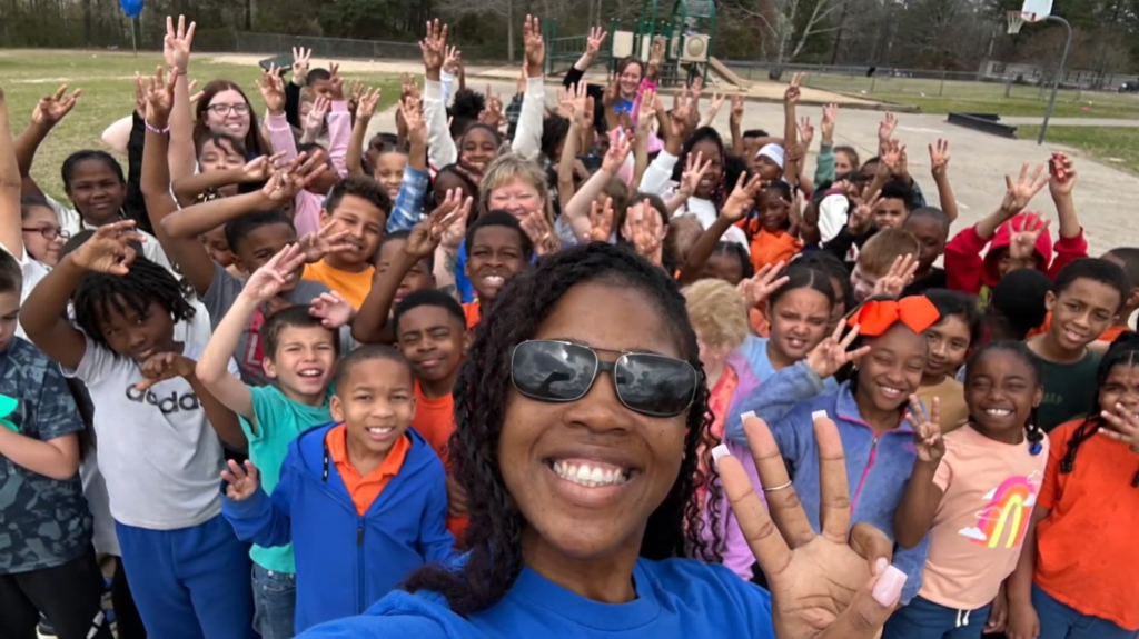Group photo outside of several students and their teacher outside making a "W" sign with their hands