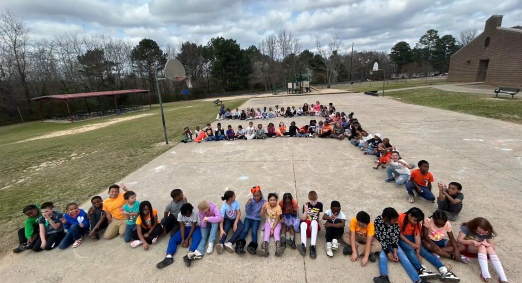 Students lined up in an "E" shape sitting on the ground outside