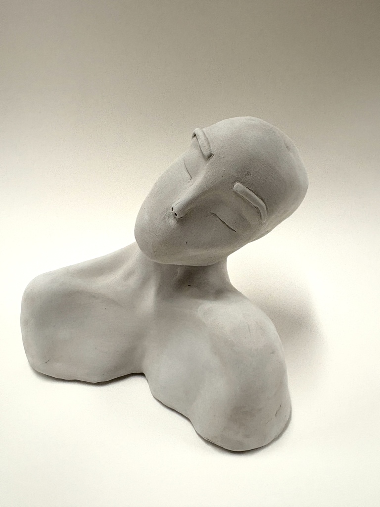 A smooth, light-colored clay bust with simplified features. The head tilts slightly to one side with closed eyes, giving the sculpture a calm, contemplative expression.