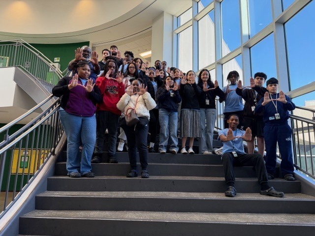 IMG_0828A group of AVID students stand on a staircase inside the school, many holding their hands in a “U” shape as they pose for a group photo.