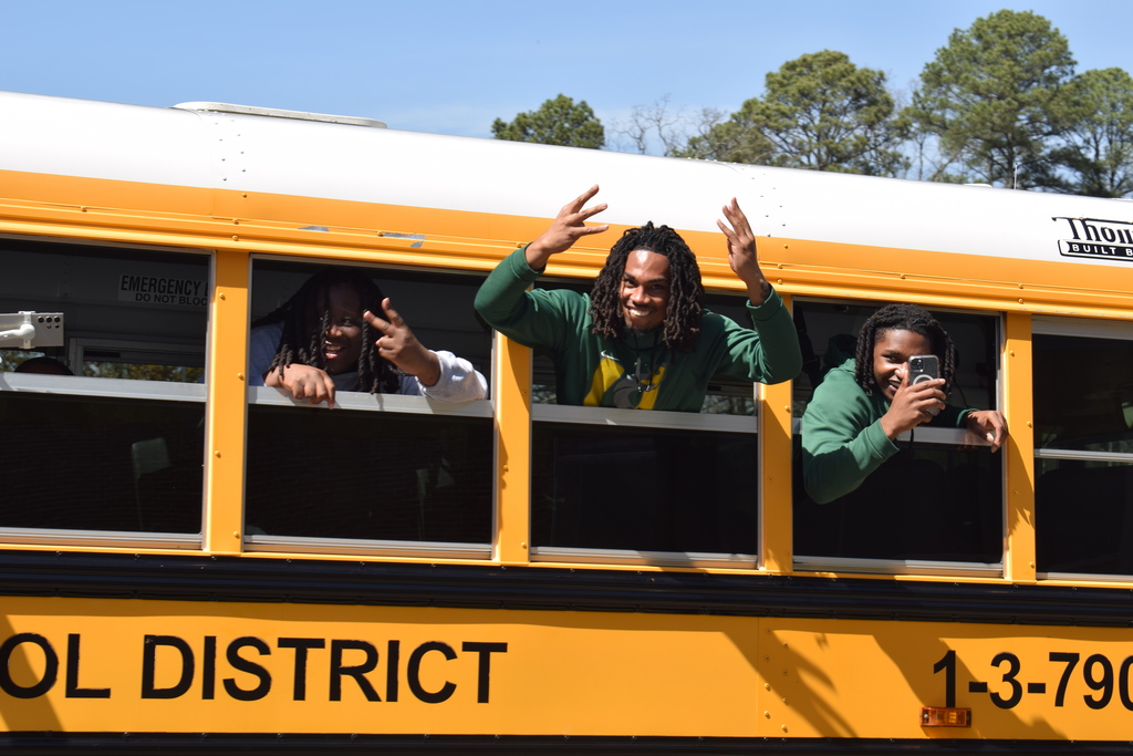 Three students looking at the camera outside the bus