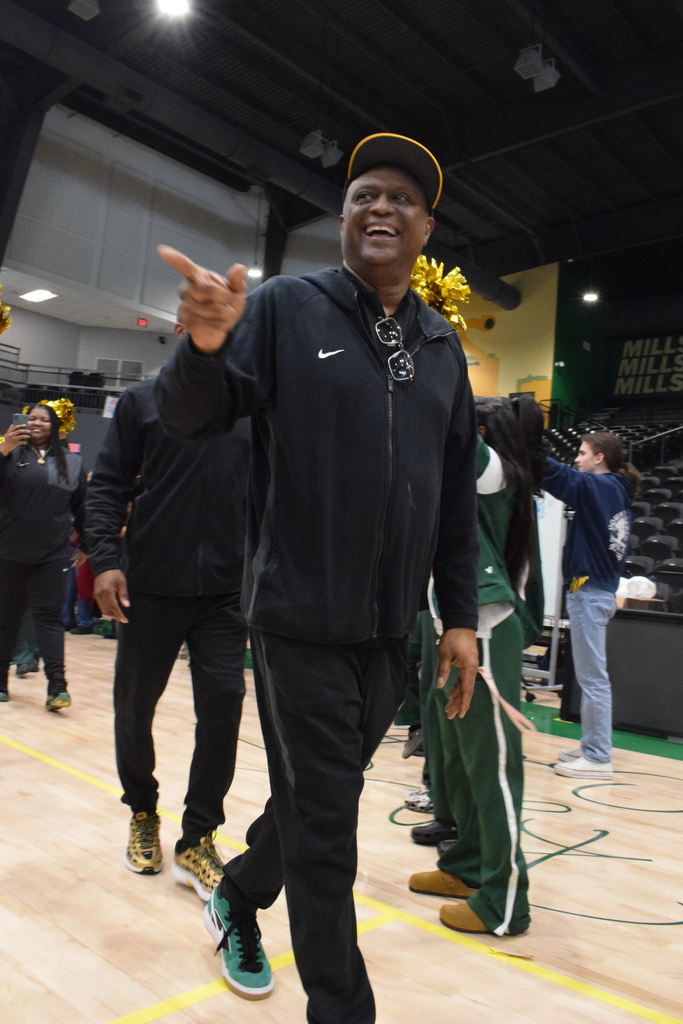 A basketball coach smiling and pointing to the crowd.