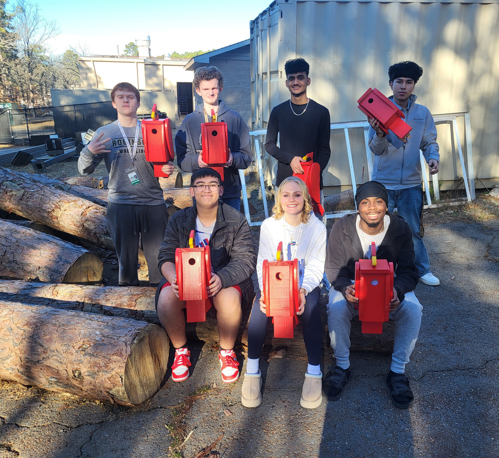Mr. Wadell's class seated on logs similar to those harvested for the birdhouses.