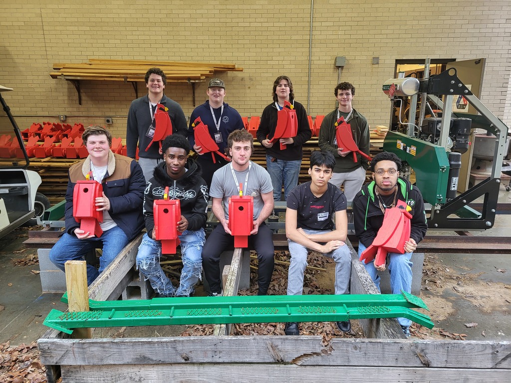 RHS students are sitting in front of the sawmill that was used to process the wood for the birdhouses. 