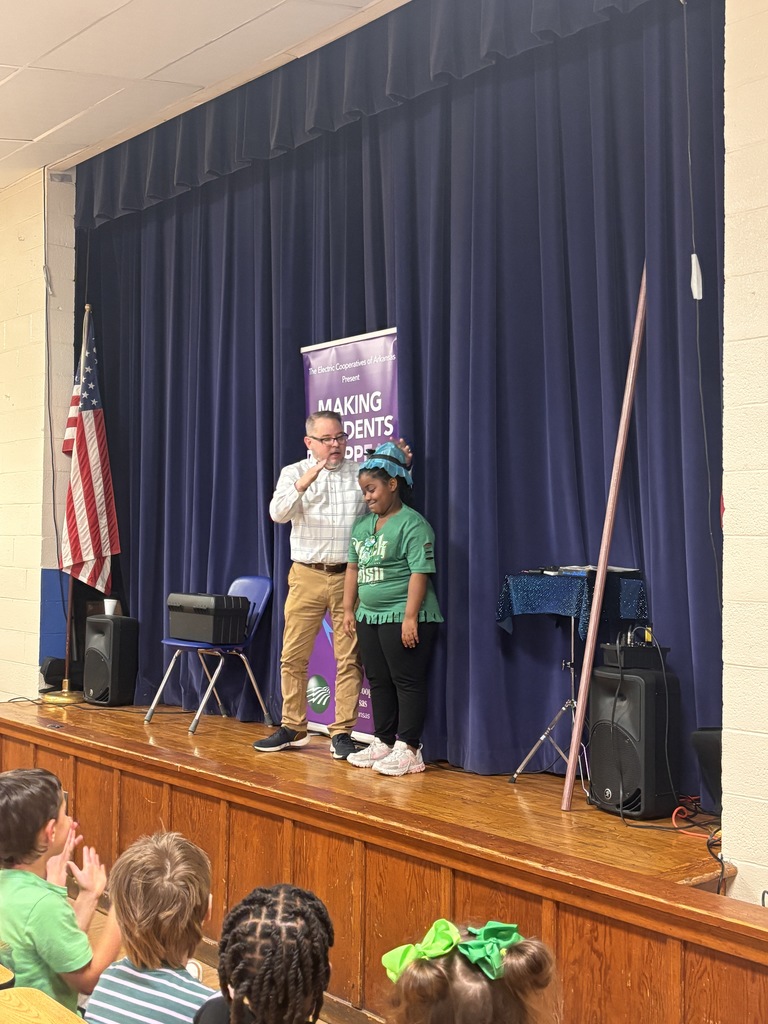 Scott Davis in front our Lawson Students explaining what his show is all about (electrical safety). He is on stage with a banner behind him that reads "making accidents disappear". He has a student helper who is wearing a green "lucky me" shirt.  The paper she was holding in previous photos was "magically" transformed into a hat.