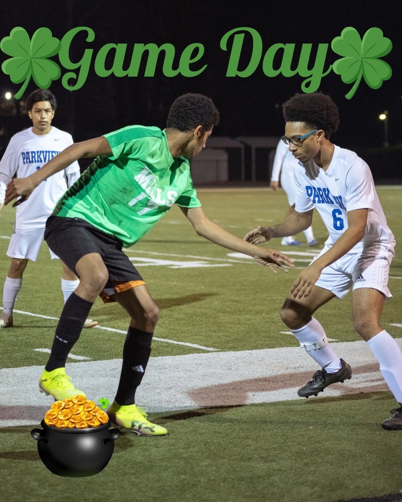 A Mills player in a green jersey dribbles past a Parkview defender during a nighttime soccer match. “Game Day” with shamrocks and a pot of gold graphic are added to the image.