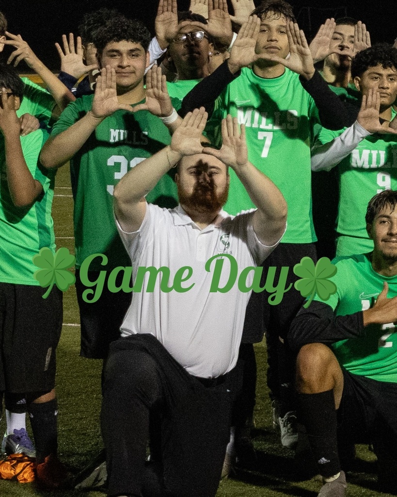 Alt text: Mills soccer players and their coach pose together on the field at night, many making "U" hand signs. “Game Day” with shamrocks is overlaid on the image.