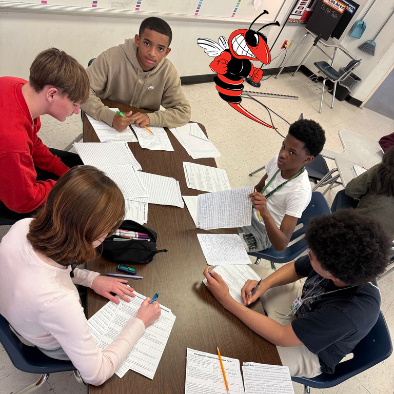 Five students sit around a table reviewing persuasive essays. A red and black hornet mascot graphic floats above them. Worksheets include peer review questions about argument structure and evidence.