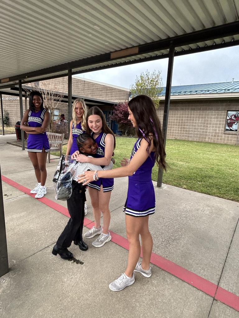 UCA Cheer Squad members greet families outside Crystal Hill Elementary. A student is hugging one  cheerleader and is about to hug another.