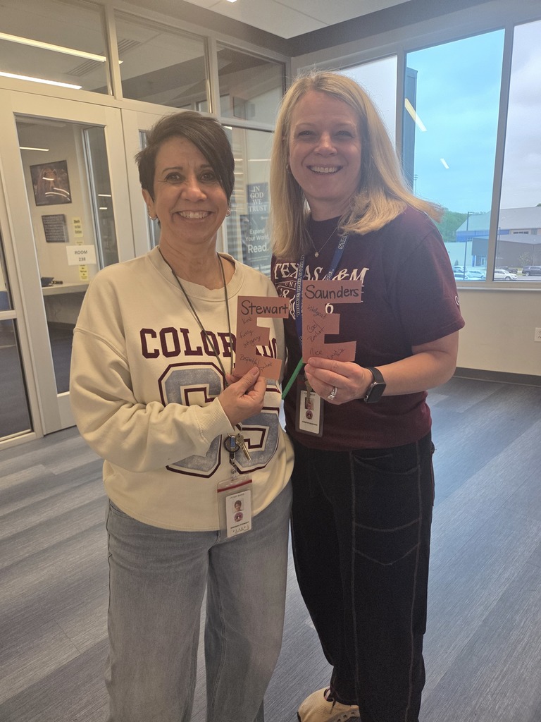 Two Sylvan Hills High School teachers smiling while holding up a brown paper letter 'E', an April Fools' prank filled with positive messages from students.