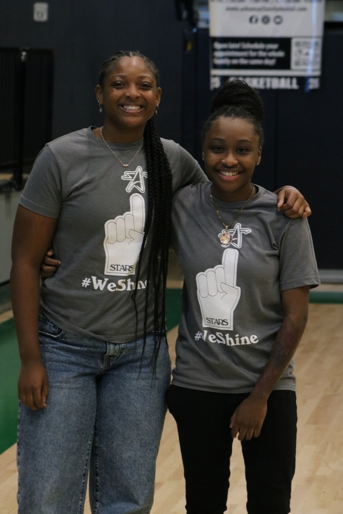 Two people stand in a gym wearing gray “STARS #WeShine” shirts as they pose together.
