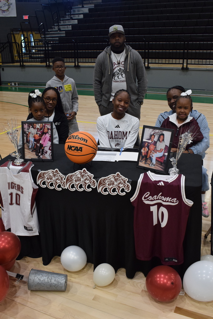 Six people gather around a table on a basketball court for a signing ceremony. The table displays Coahoma and Tigers jerseys, a basketball, framed photos, and tiger decorations.
