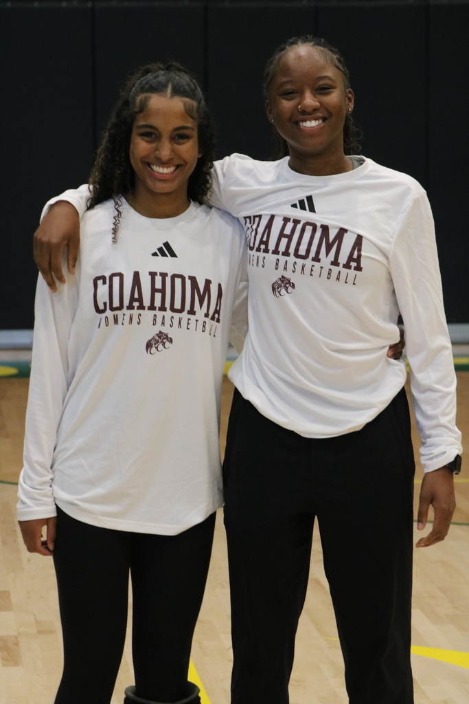 Two people stand in a gym wearing white “Coahoma Women’s Basketball” shirts as they pose together.
